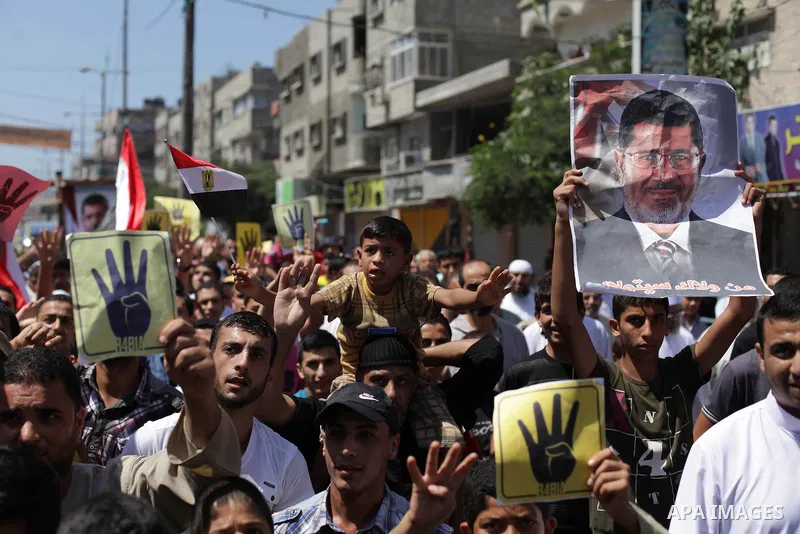 Palestinians hold Egyptian national flags, posters of ousted Egyptian President Mohamed Morsi and logos of four fingers, during a demonstration to support Morsi and denounce Syria's President Bashar al-Assad, in Al-Nusir...