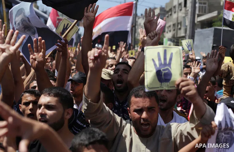Palestinians hold Egyptian national flags, posters of ousted Egyptian President Mohamed Morsi and logos of four fingers, during a demonstration to support Morsi and denounce Syria's President Bashar al-Assad, in Al-Nusir...