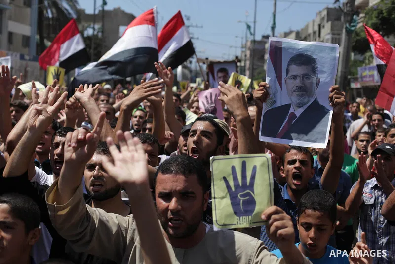 Palestinians hold Egyptian national flags, posters of ousted Egyptian President Mohamed Morsi and logos of four fingers, during a demonstration to support Morsi and denounce Syria's President Bashar al-Assad, in Al-Nusir...