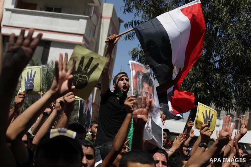 Palestinians hold Egyptian national flags, posters of ousted Egyptian President Mohamed Morsi and logos of four fingers, during a demonstration to support Morsi and denounce Syria's President Bashar al-Assad, in Al-Nusir...