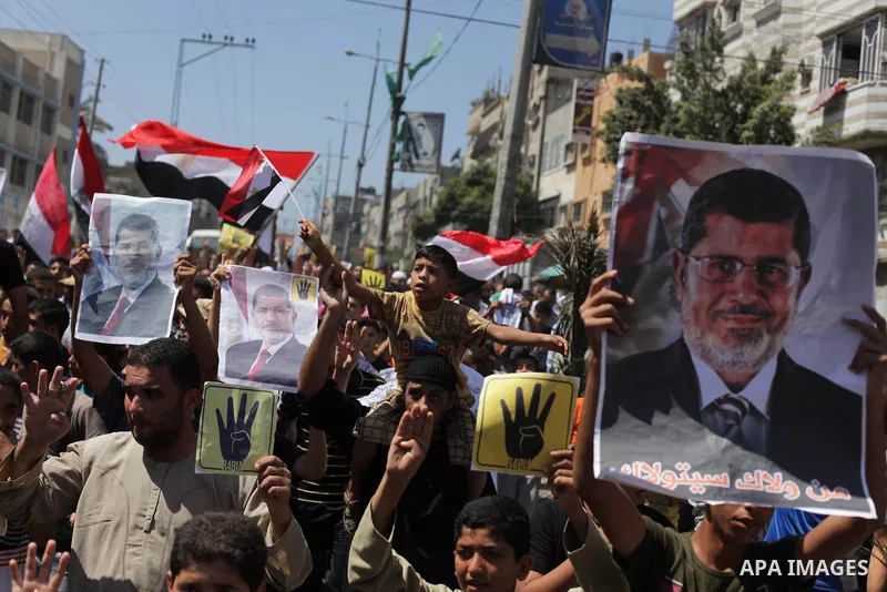 Palestinians hold Egyptian national flags, posters of ousted Egyptian President Mohamed Morsi and logos of four fingers, during a demonstration to support Morsi and denounce Syria's President Bashar al-Assad, in Al-Nusir...