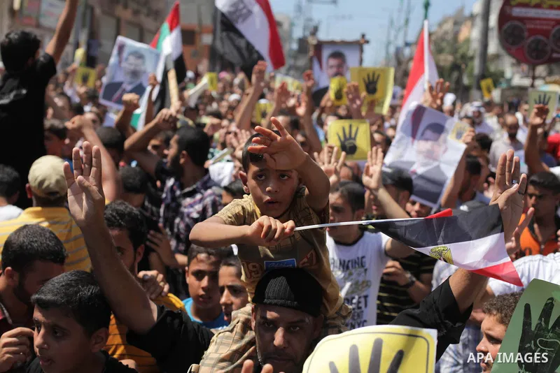 Palestinians hold Egyptian national flags, posters of ousted Egyptian President Mohamed Morsi and logos of four fingers, during a demonstration to support Morsi and denounce Syria's President Bashar al-Assad, in Al-Nusir...