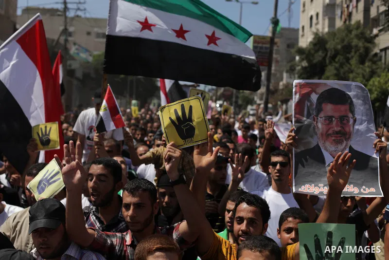 Palestinians hold Egyptian national flags, posters of ousted Egyptian President Mohamed Morsi and logos of four fingers, during a demonstration to support Morsi and denounce Syria's President Bashar al-Assad, in Al-Nusir...