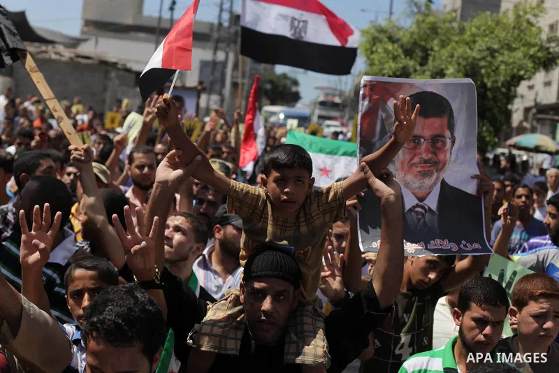 Palestinians hold Egyptian national flags, posters of ousted Egyptian President Mohamed Morsi and logos of four fingers, during a demonstration to support Morsi and denounce Syria's President Bashar al-Assad, in Al-Nusir...