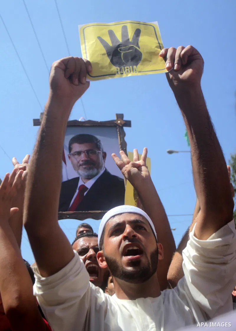 Palestinians hold Egyptian national flags, posters of ousted Egyptian President Mohamed Morsi and logos of four fingers, during a demonstration to support Morsi and denounce Syria's President Bashar al-Assad, in Al-Nusir...