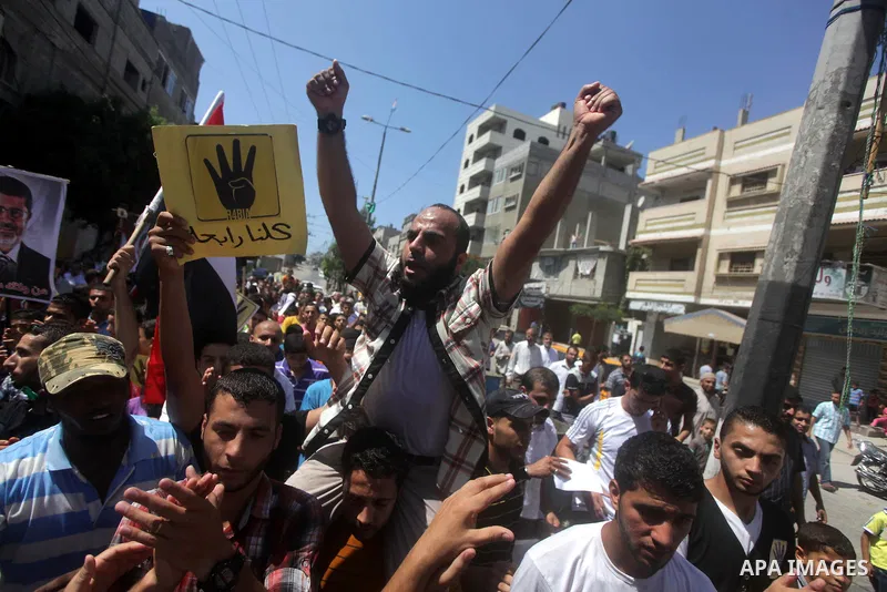 Palestinians hold Egyptian national flags, posters of ousted Egyptian President Mohamed Morsi and logos of four fingers, during a demonstration to support Morsi and denounce Syria's President Bashar al-Assad, in Al-Nusir...