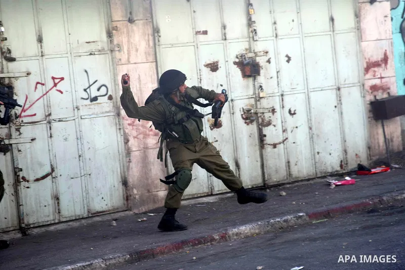 An Israeli soldier throws a stun grenade at Palestinian protesters during clashes following a protest against Israeli settlements on August 27,2013 in the city center of the West Bank town of Hebron. Israeli-Palestinian...