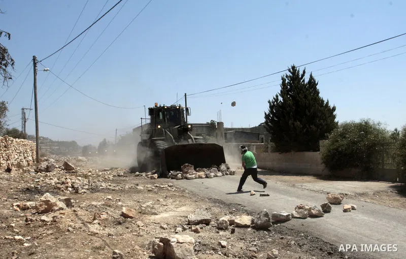 A Palestinian protester throws stones at Israeli bulldozer during clashes following a protest against the expropriation of Palestinian land by Israel in the village of Kfar Qaddum, near Nablus in the occupied West Bank o...
