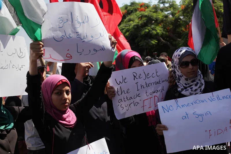 Palestinians hold banners and wave the Syrian flag as they take part in a rally, organized by the Palestinian leftist party, the Popular Front for the Liberation of Palestine (PFLP), against US military action on Syria,...