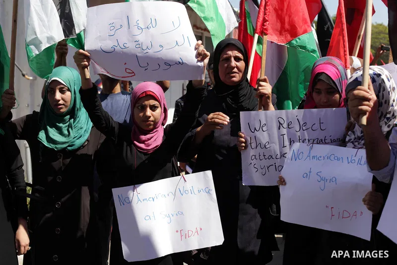 Palestinians hold banners and wave the Syrian flag as they take part in a rally, organized by the Palestinian leftist party, the Popular Front for the Liberation of Palestine (PFLP), against US military action on Syria,...