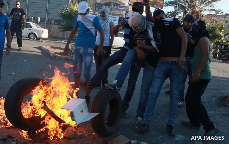 Palestinian protesters stand next to burning tires during clashes with Israeli soldiers in north of Jerusalem city on September 27, 2013. Thousands of Palestinians demonstrated in the Gaza Strip, the West Bank and east J...