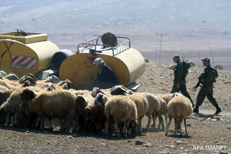 Israeli soldiers walk past a Palestinian Bedouin man as he irrigates sheep from a water container in the Jordan valley village of Makhoul September 30, 2013. Israel's army on Monday declared the Jordan Valley village of...