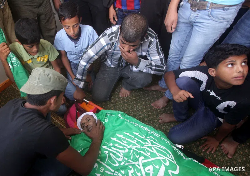 Palestinians sit next to the body of Palestinian Heweshil Abu Heweshil, who was killed by Israeli soldiers, during his funeral in center Gaza City October 1, 2013. Israeli soldiers shot dead Abu Heweshil near the border...