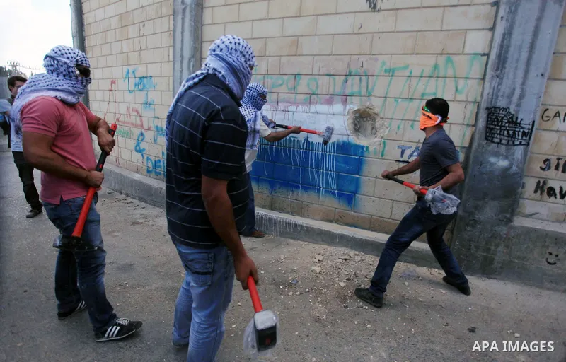 Palestinian activists use hammers to smash holes in the Israel separation barrier in the West Bank town of Abu Dis next to Jerusalem, October 03, 2013. The Activity was initiated by the Popular Committees Against the wal...