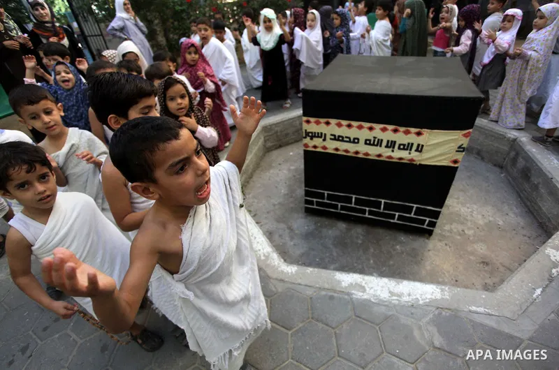Palestinian children gather around a makeshift cube representing the holy Kaaba in Gaza city, on October 12, 2013, as part of training children how to perform Hajj pilgrimage. Muslims from around the world flood Saudi ci...