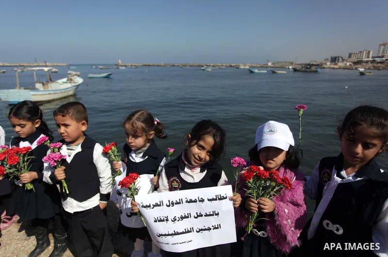 Palestinian school children throw flowers into the Seaport of Gaza City October 23, 2013, to remember the Palestinian migrants who died after their boat sank while fleeing Syria to Italy. A boat capsized 60 miles south o...