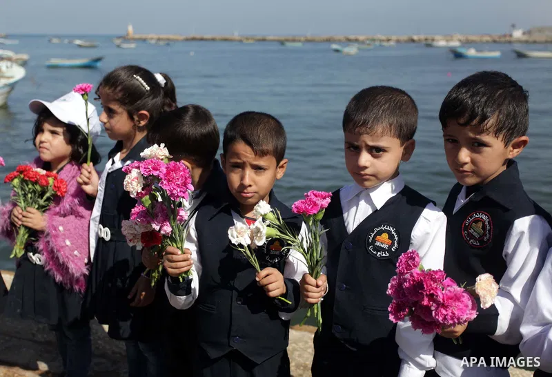 Palestinian school children throw flowers into the Seaport of Gaza City October 23, 2013, to remember the Palestinian migrants who died after their boat sank while fleeing Syria to Italy. A boat capsized 60 miles south o...