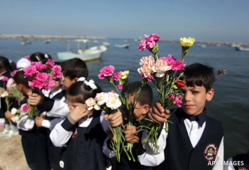 Palestinian school children throw flowers into the Seaport of Gaza City October 23, 2013, to remember the Palestinian migrants who died after their boat sank while fleeing Syria to Italy. A boat capsized 60 miles south o...