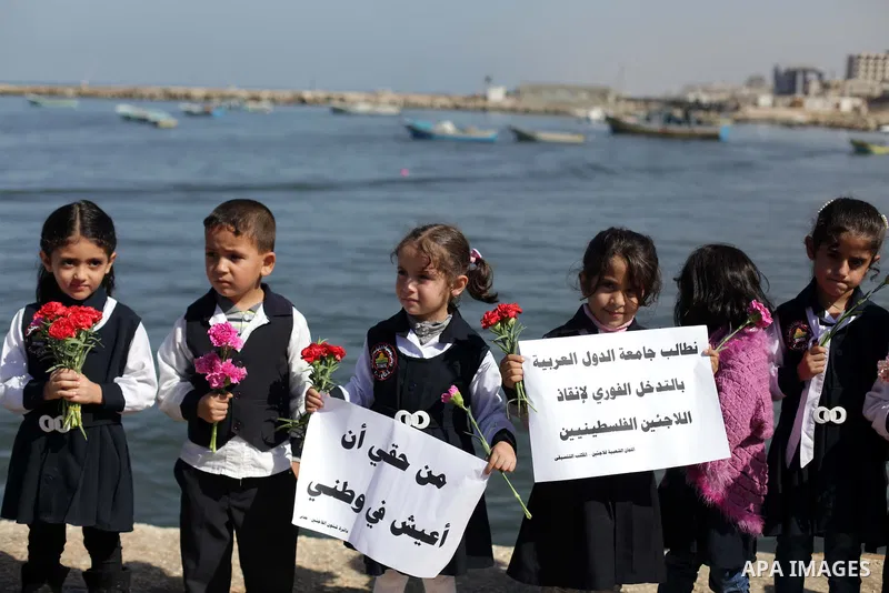 Palestinian school children throw flowers into the Seaport of Gaza City October 23, 2013, to remember the Palestinian migrants who died after their boat sank while fleeing Syria to Italy. A boat capsized 60 miles south o...