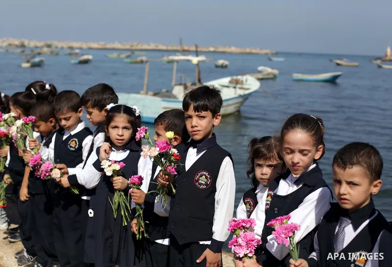 Palestinian school children throw flowers into the Seaport of Gaza City October 23, 2013, to remember the Palestinian migrants who died after their boat sank while fleeing Syria to Italy. A boat capsized 60 miles south o...