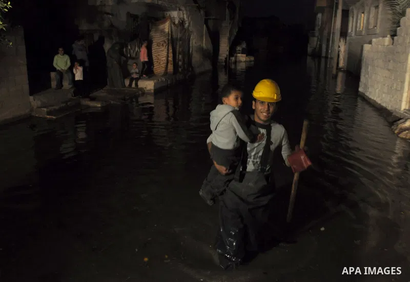 A Palestinian worker carries a boy as he walks in a flooded street with sewage in al-Sabra neighborhood, in Gaza City on November 13, 2013. The main pump of sewage water which serves thousands of citizens in a densely po...