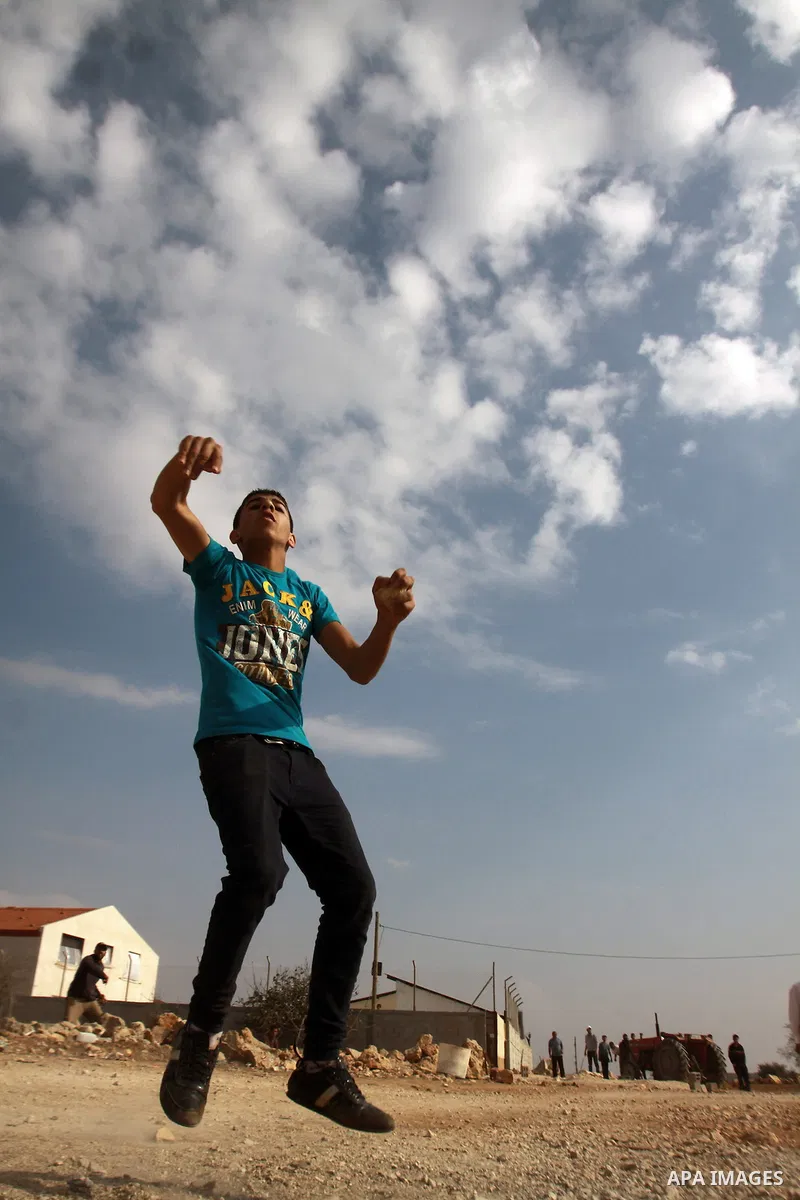 A Palestinian youth throws stones at Israeli army jeeps during clashes following a confrontation between Palestinians and Jewish settlers, in the West Bank village of Qusra, near Nablus, November 18, 2013. Jewish settler...