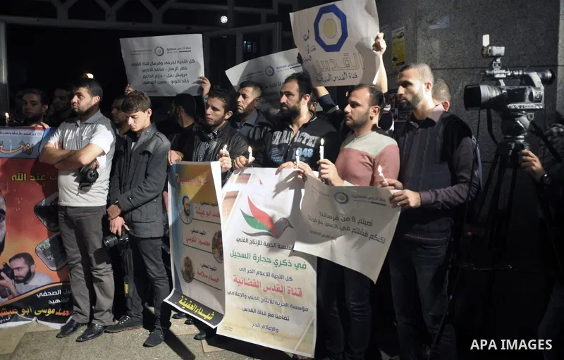 Palestinian journalists hold placards and candles during a protest in solidarity with the local al-Quds TV on the first anniversary of targeting their offices by Israeli warplanes, in Gaza City on November 18, 2013. The...