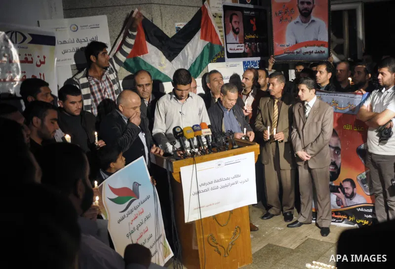 Palestinian journalists hold placards and candles during a protest in solidarity with the local al-Quds TV on the first anniversary of targeting their offices by Israeli warplanes, in Gaza City on November 18, 2013. The...