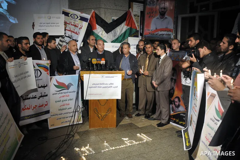 Palestinian journalists hold placards and candles during a protest in solidarity with the local al-Quds TV on the first anniversary of targeting their offices by Israeli warplanes, in Gaza City on November 18, 2013. The...