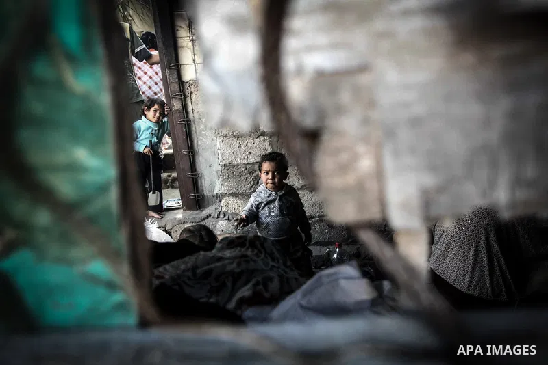 Palestinian children play as their mother bakes bread on firewood at her tin shack in Khan Younis refugee camp, in southern Gaza Strip, November 21, 2013. The UNRWA, which is facing a 36-million dollar deficit, halted 19...