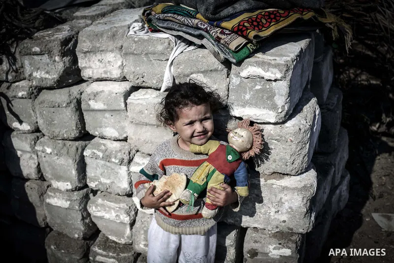 A Palestinian girl holds a loaf of bread outside her tin shack in Khan Younis refugee camp, in southern Gaza Strip, November 21, 2013. The UNRWA, which is facing a 36-million dollar deficit, halted 19 out of 20 construct...
