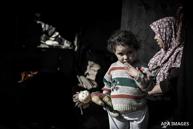 A Palestinian girl holds a loaf of bread as her mother bakes on firewood at her tin shack in Khan Younis refugee camp, in southern Gaza Strip, November 21, 2013. The UNRWA, which is facing a 36-million dollar deficit, ha...