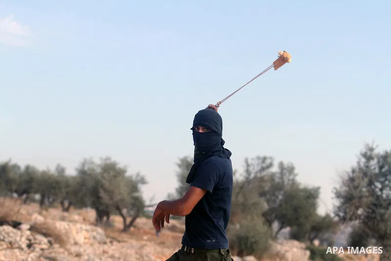 A masked Palestinian protester hurls a stone at Israeli border policemen during the weekly demonstration against Israel's separation barrier in the West Bank village of Bilin, near Ramallah, Friday, Nov. 22, 2013. Photo...