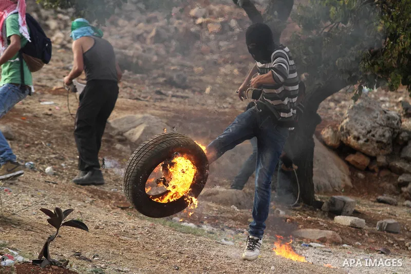 A Palestinian protester kicks a burning tyre during clashes between students from Bir Zeit University and Israeli security forces in the West Bank village of Betunia following a protest against the killing of three young...