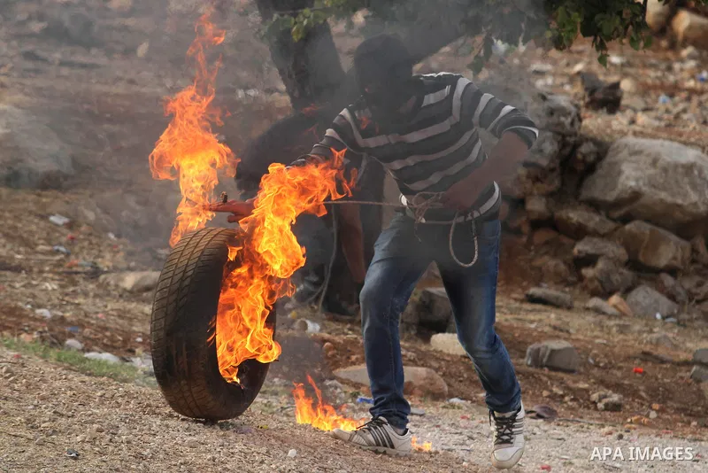 A Palestinian holds kicks a burning tyre during clashes between students from Bir Zeit University and Israeli security forces in the West Bank village of Betunia following a protest against the killing of three young Pal...