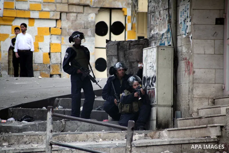 An Israeli soldier aims his gun towards Palestinian protesters during clashes in the West bank city of Hebron, 27 November 2013. The clashes began after the killing of three Palestinians militants in the West bank villag...