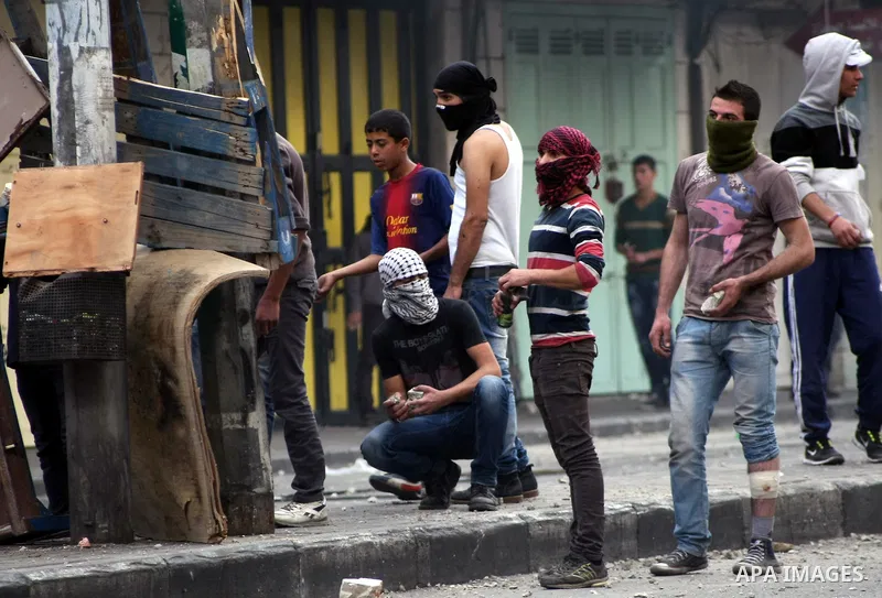 Palestinian protesters throw stones at Israeli soldiers during clashes in the West bank city of Hebron, 27 November 2013. The clashes began after the killing of three Palestinians militants in the West bank village of Ya...