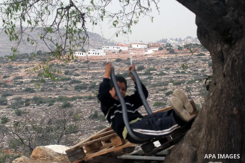 A Palestinian boy from the village of al-Mazraa al-Kubliyeh plays on a swing as bungalows built by Israeli settlers at an outpost constructed on seized land from the Palestinian village are seen in the background, near t...