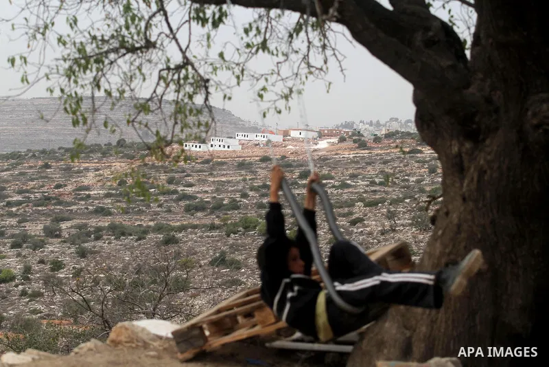 A Palestinian boy from the village of al-Mazraa al-Kubliyeh plays on a swing as bungalows built by Israeli settlers at an outpost constructed on seized land from the Palestinian village are seen in the background, near t...
