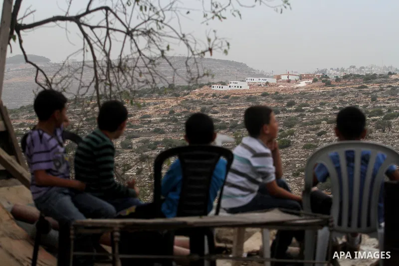 Palestinian children from the village of al-Mazraa al-Kubliyeh look a bungalows in the distance built by Israeli settlers at an outpost constructed on seized land from the Palestinian village, near the West Bank city of...