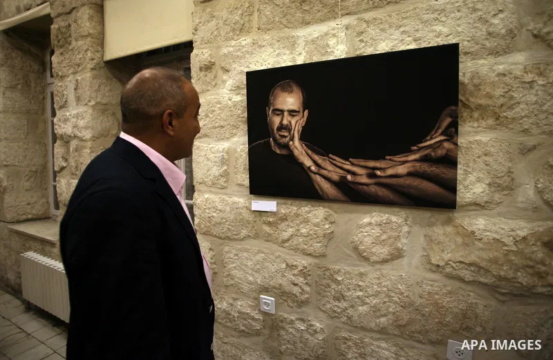 A Palestinian man looks at a photo during a photogallery named 'Room Four', organised by French culture center in Jerusalem on Dec. 05, 2013. The photos by the artist Ashraf Dowani displayed in the photogallery and refle...