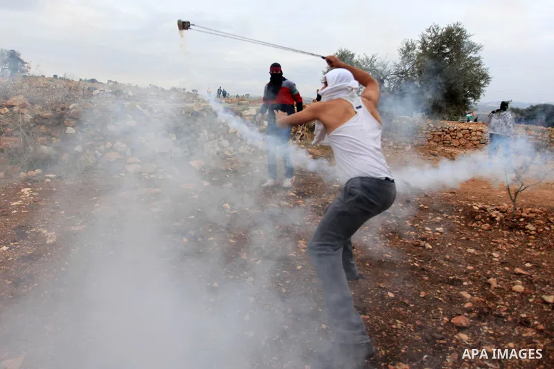 A Palestinian protester uses a slingshot to throw a tear gas canister towards Israeli soldiers during clashes between youths and the army following a weekly protest against Israeli occupation in the West Bank village of...