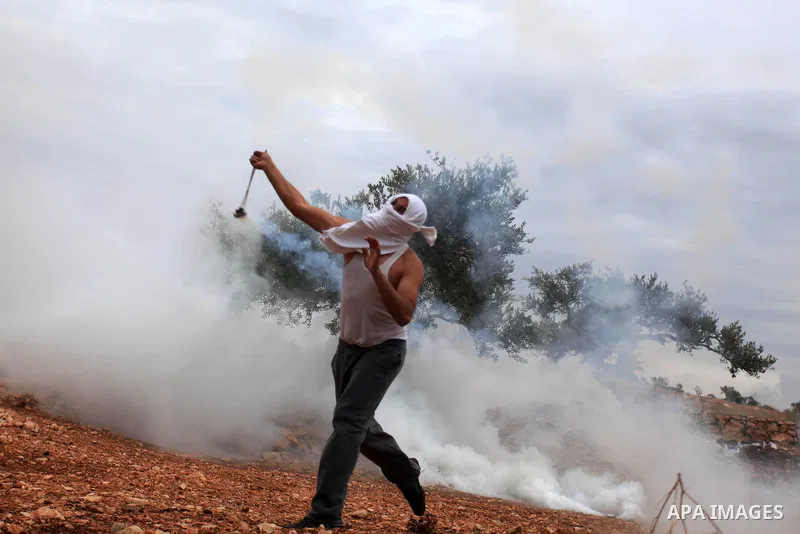 A Palestinian protester uses a slingshot to throw a tear gas canister towards Israeli soldiers during clashes between youths and the army following a weekly protest against Israeli occupation in the West Bank village of...