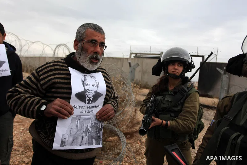 A Palestinian man holds a portrait of late South African president Nelson Mandela as he stands in front of Israeli soldiers during clashes between youths and the army following a weekly protest against Israeli occupation...