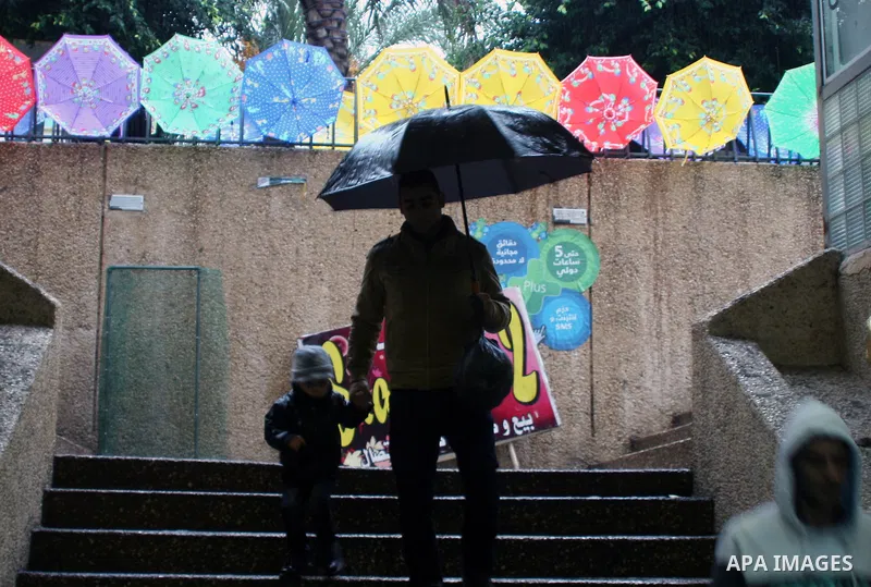Palestinians walk pass umbrellas displayed for sale during a downpour, in the West Bank City of Nablus, Dec. 08, 2013. Photo by Nedal Eshtayah