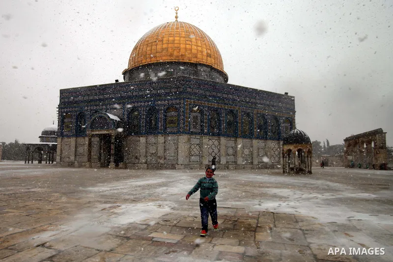 A Palestinian boy plays in the snow in front of the Dome of the Rock at the Al-Aqsa mosques compound in the old city of Jerusalem on December 12, 2013 as a winter weather front hit the region, bringing early snow and a s...