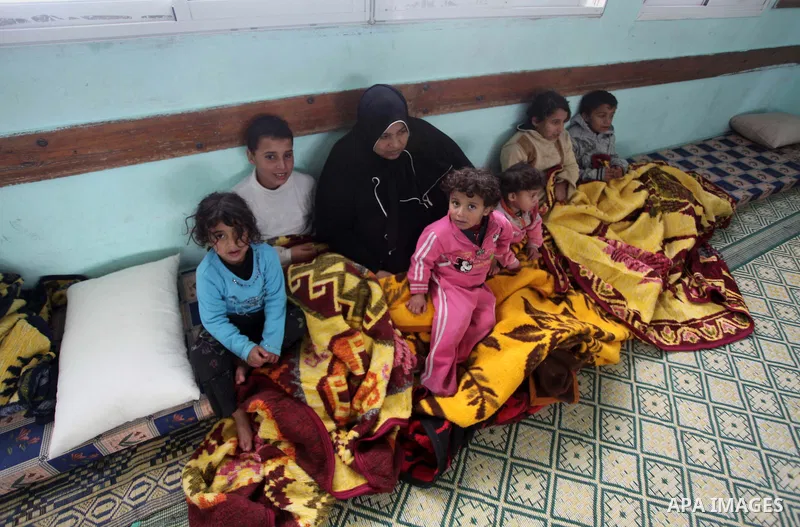 A Palestinian woman sits with her children at a school after being evacuated from their house that is flooded with rainwater, on a stormy day in Khan Younis in the southern Gaza Strip December 12, 2013. Photo by Ashraf A...