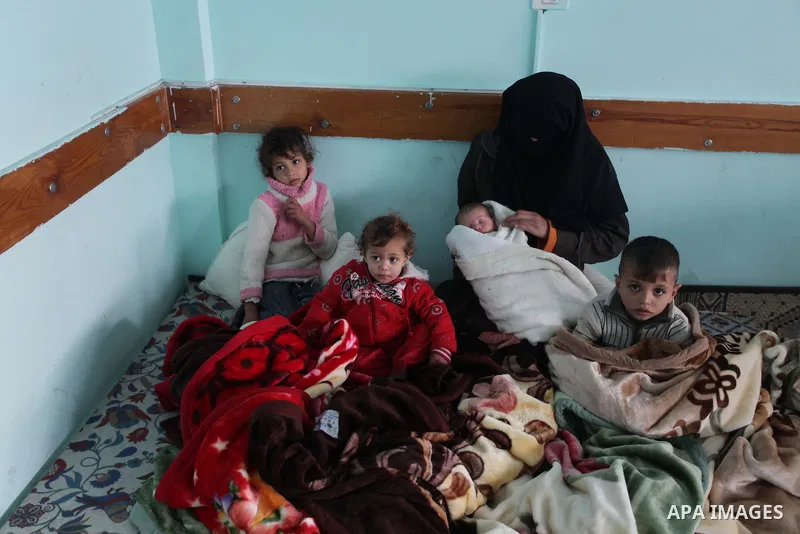 A Palestinian woman sits with her children at a school after being evacuated from their house that is flooded with rainwater, on a stormy day in Khan Younis in the southern Gaza Strip December 12, 2013. Photo by Ashraf A...
