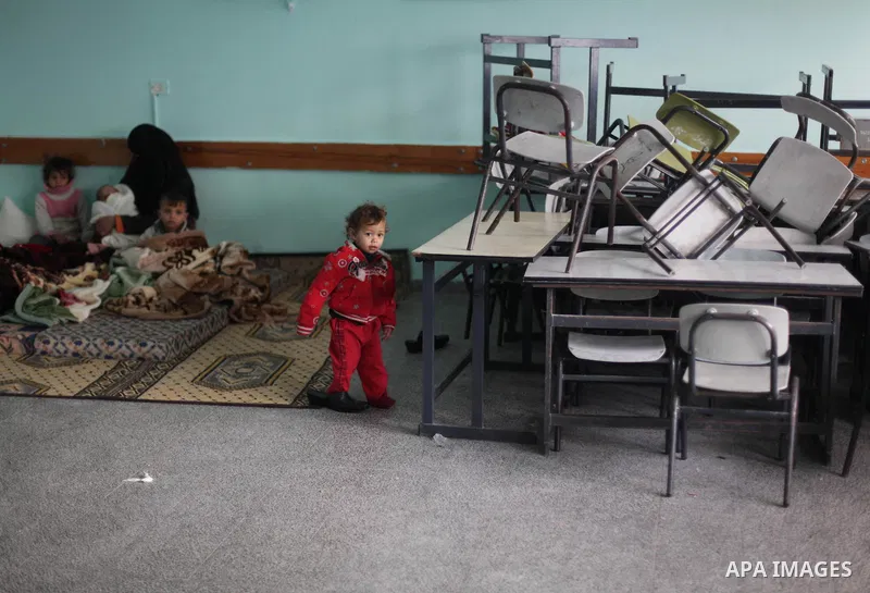 A Palestinian woman sits with her children at a school after being evacuated from their house that is flooded with rainwater, on a stormy day in Khan Younis in the southern Gaza Strip December 12, 2013. Photo by Ashraf A...