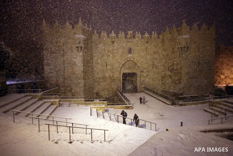 People walk in front of Damascus gate during a snowstorm in Jerusalem's Old City on December 12, 2013. Jerusalem is covered with snow Thursday, the heaviest snow storm hitting the city since 1953 as meteorologists dubbed...